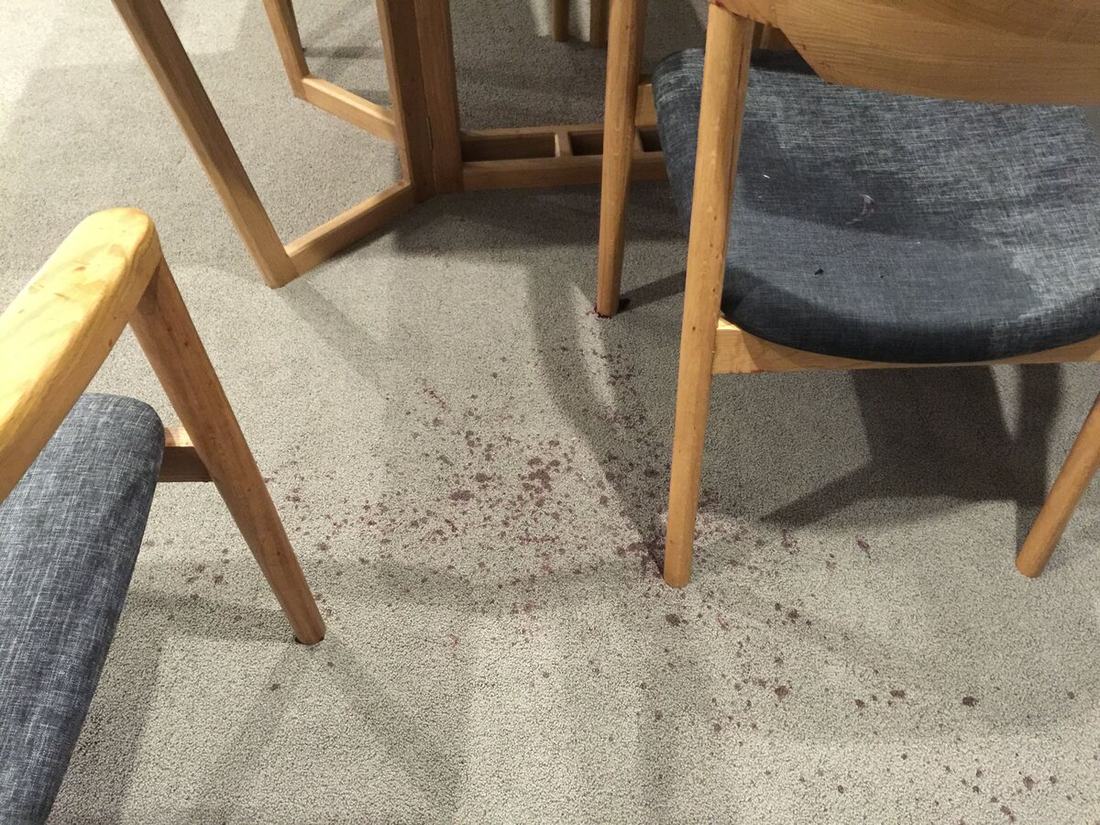 Red wine splatter across wool carpet under a dining table